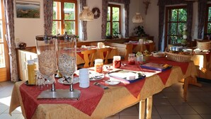 Un comedor con una mesa lista para el desayuno, que incluye una cesta de fruta, pan y diferentes alimentos para el desayuno.