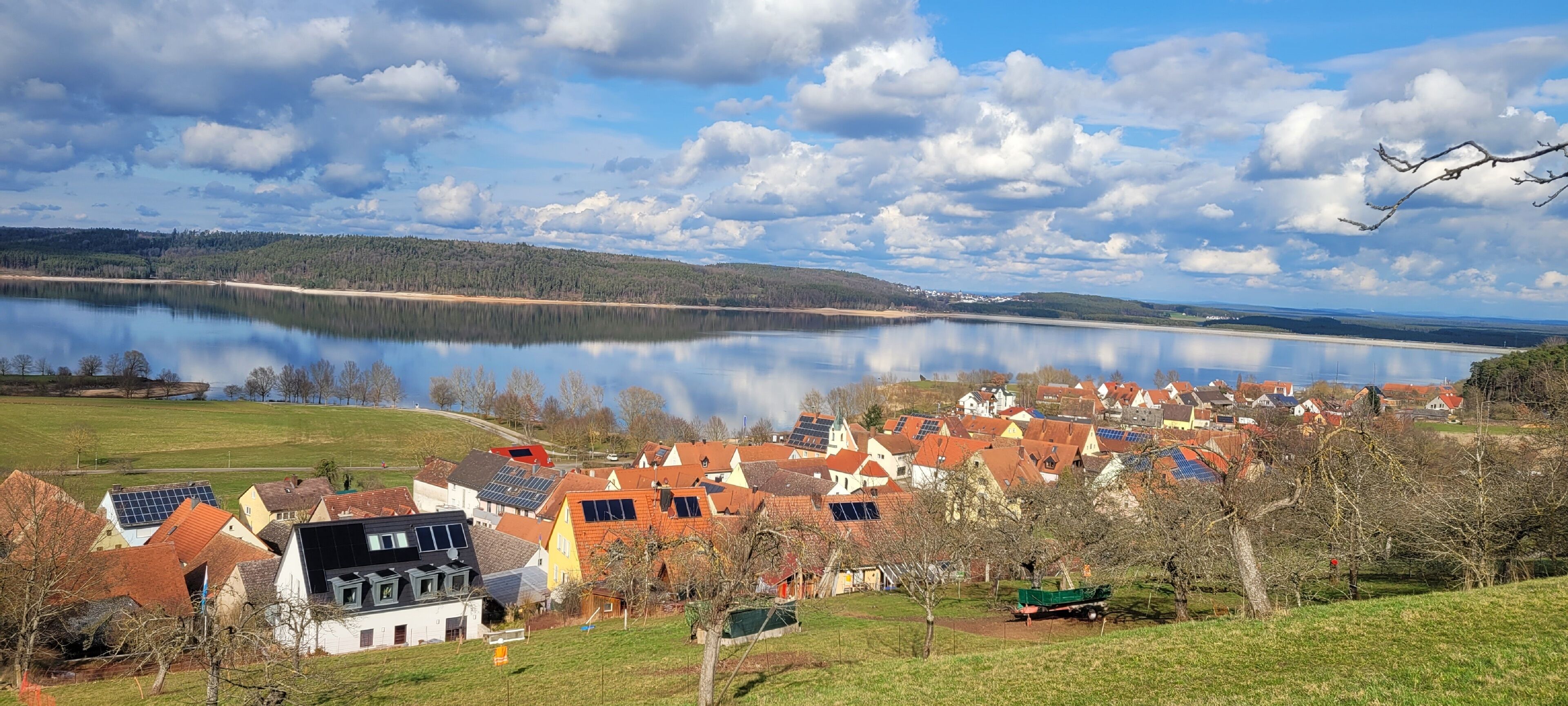 Ein Dorf am See mit Häusern, einem See und einem bewaldeten Hügel im Hintergrund.