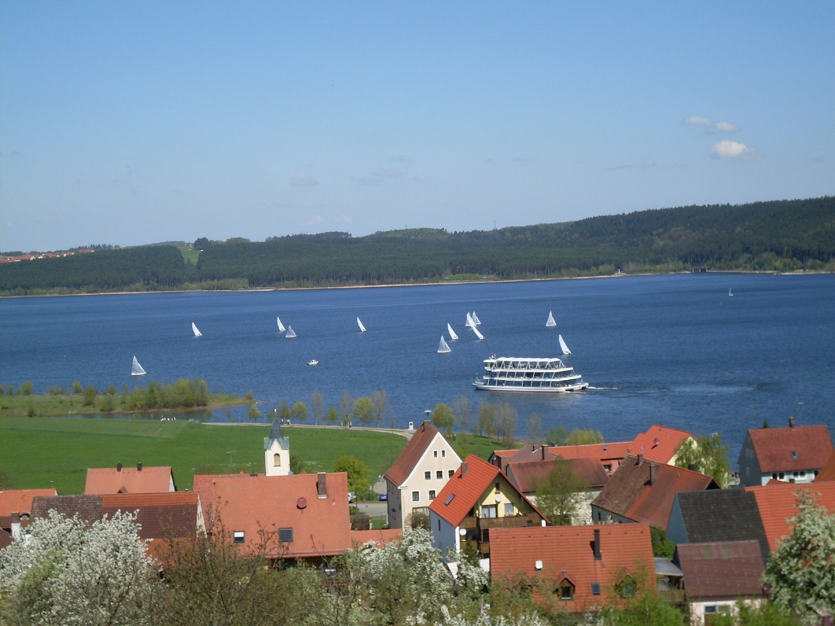 A lake with sailboats and a houseboat in the foreground.