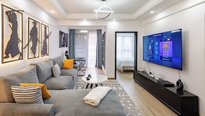A modern living room with a grey sofa, a coffee table, and a flat-screen TV displaying a sports channel. - Modern 1-bedroom Apartment in Vibrant Westlands, Nairobi (Nairobi)