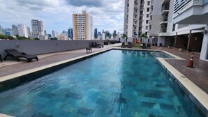 Una piscina en la azotea con sillones de descanso y un horizonte urbano al fondo.