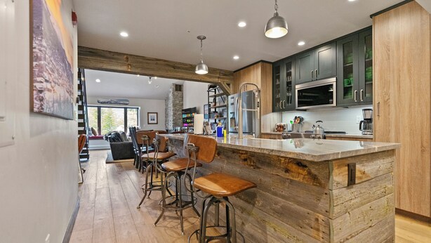 A modern kitchen with wooden accents, a bar area with stools, and a stone fireplace.
