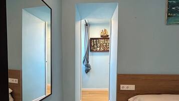 Ein Zimmer mit einem Bett, einem Spiegel, einem kleinen Fenster mit Vorhang und einer Wanddekoration.