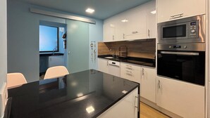 Uma cozinha moderna com armários brancos, bancada preta, micro-ondas embutido e forno.