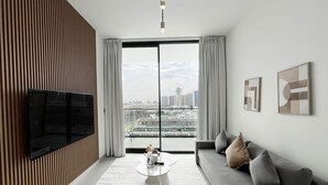 Un salon moderne doté d’un téléviseur à écran plat, d’un canapé, d’une table basse et d’une grande fenêtre offrant une vue sur la ville.