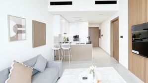 Un salon moderne avec un canapé gris, une table basse blanche et un téléviseur placé à droite.