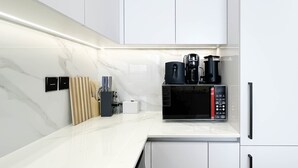 Une cuisine moderne avec des meubles blancs, un pare-feu en marbre et un four à micro-ondes encastré.