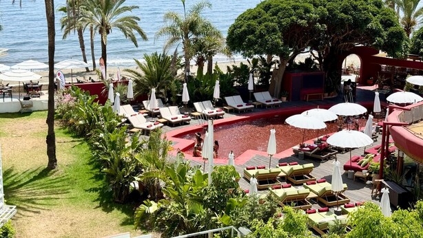 Ein Poolbereich eines Resorts mit Liegestühlen, Sonnenschirmen und Blick aufs Meer.