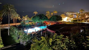 Ein Nachtblick auf einen Resort mit Pool, Palmen und Meerblick.