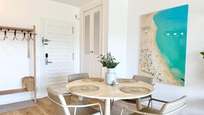 Ein Essbereich mit einem runden Tisch, vier Stühlen, einer Pflanze in einer Vase und einem Strandbild an der Wand.