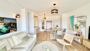 Ein modernes Wohnzimmer mit einer Couch, einem Couchtisch und einem Essbereich. An der Wand hängt ein Gemälde und rechts befindet sich ein Fernseher.