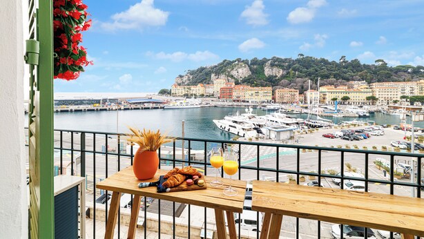 A balcony with a wooden table, a vase with dried plants, croissants, and glasses of orange juice, overlooking a marina with boats and buildings. - Sunlight Properties Archibald - Nice, 2 Beds, holiday rental, balcony & parking (Nice)