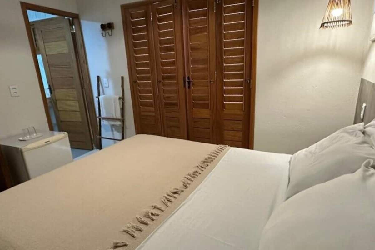 A bedroom with a bed, wooden wardrobes, a bedside table, and a wall-mounted lamp.