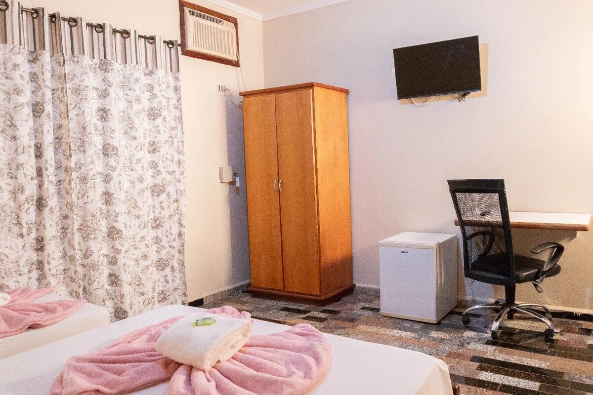 Ein Schlafzimmer mit zwei Betten, einem Kleiderschrank, einem Schreibtisch, einem Stuhl und einem kleinen weißen Gerät.