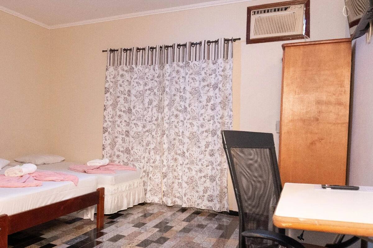 Ein Schlafzimmer mit Bett, Stuhl, Schreibtisch und einem fenster mit Vorhängen.