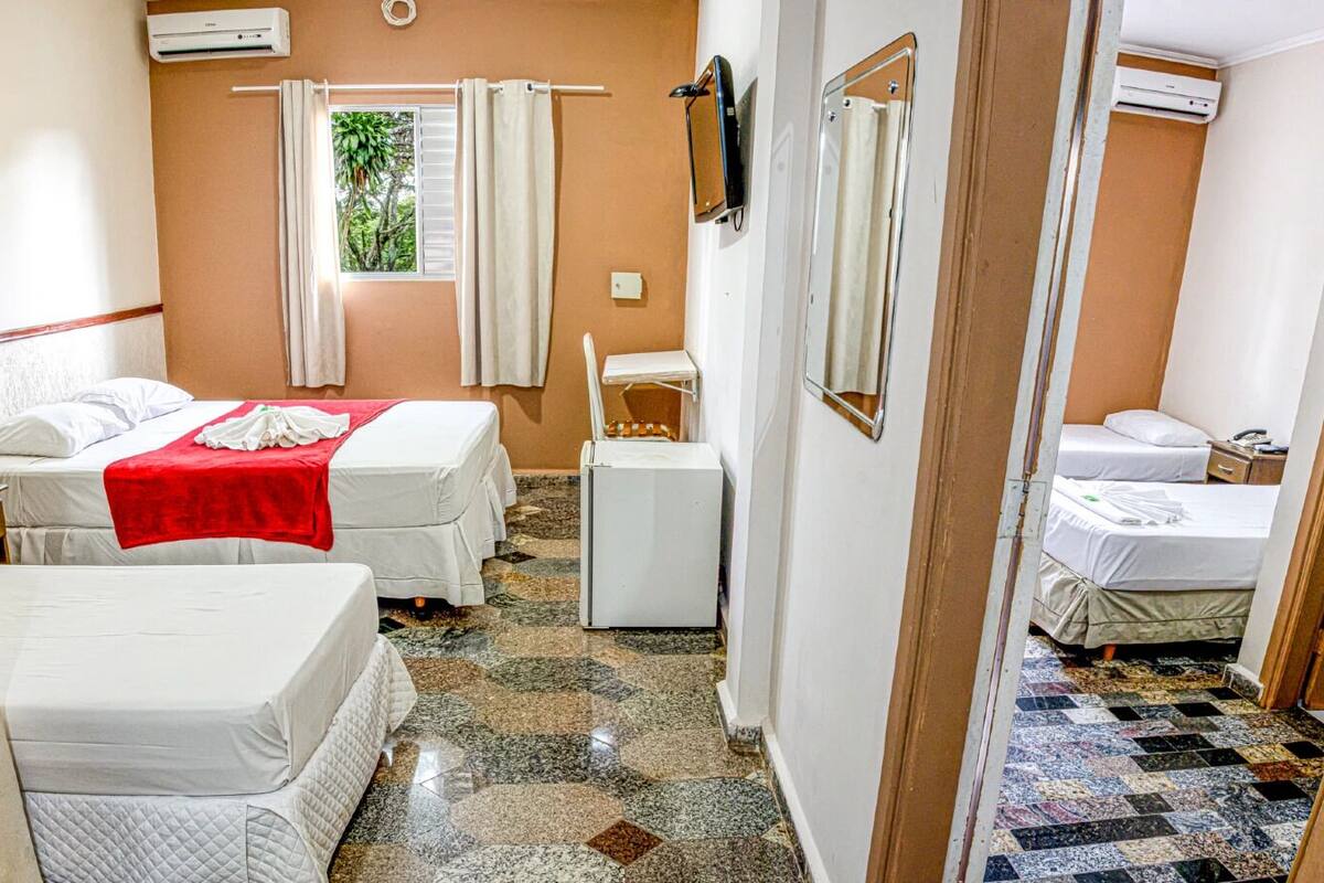 Ein Hotelzimmer mit zwei Betten, einem kleinen Tisch, einem Spiegel und einer Klimaanlage an der Wand.