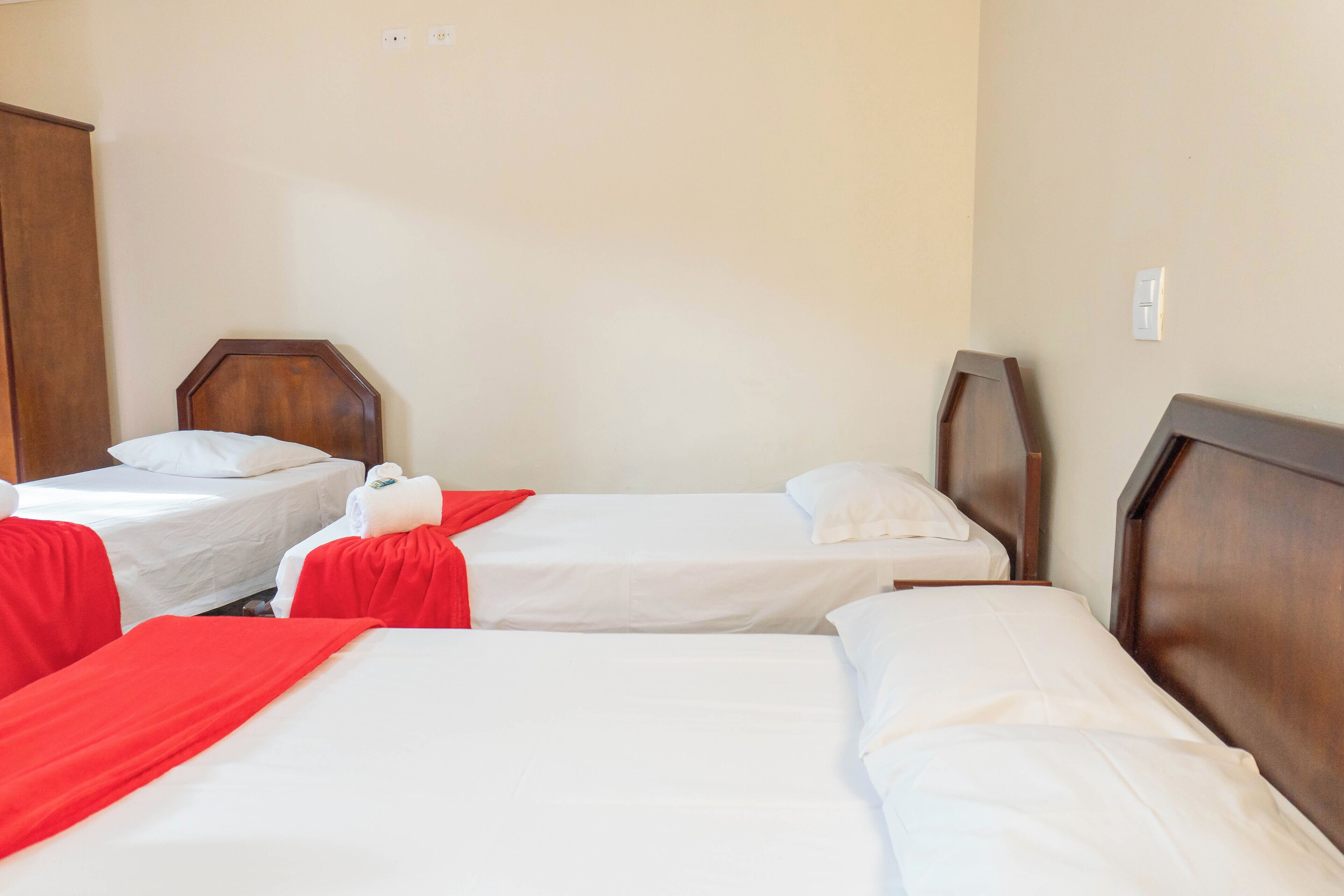 Een hotelkamer met drie eenpersoonsbedden, elk met een houten hoofdbord, wit beddengoed en rode dekens.