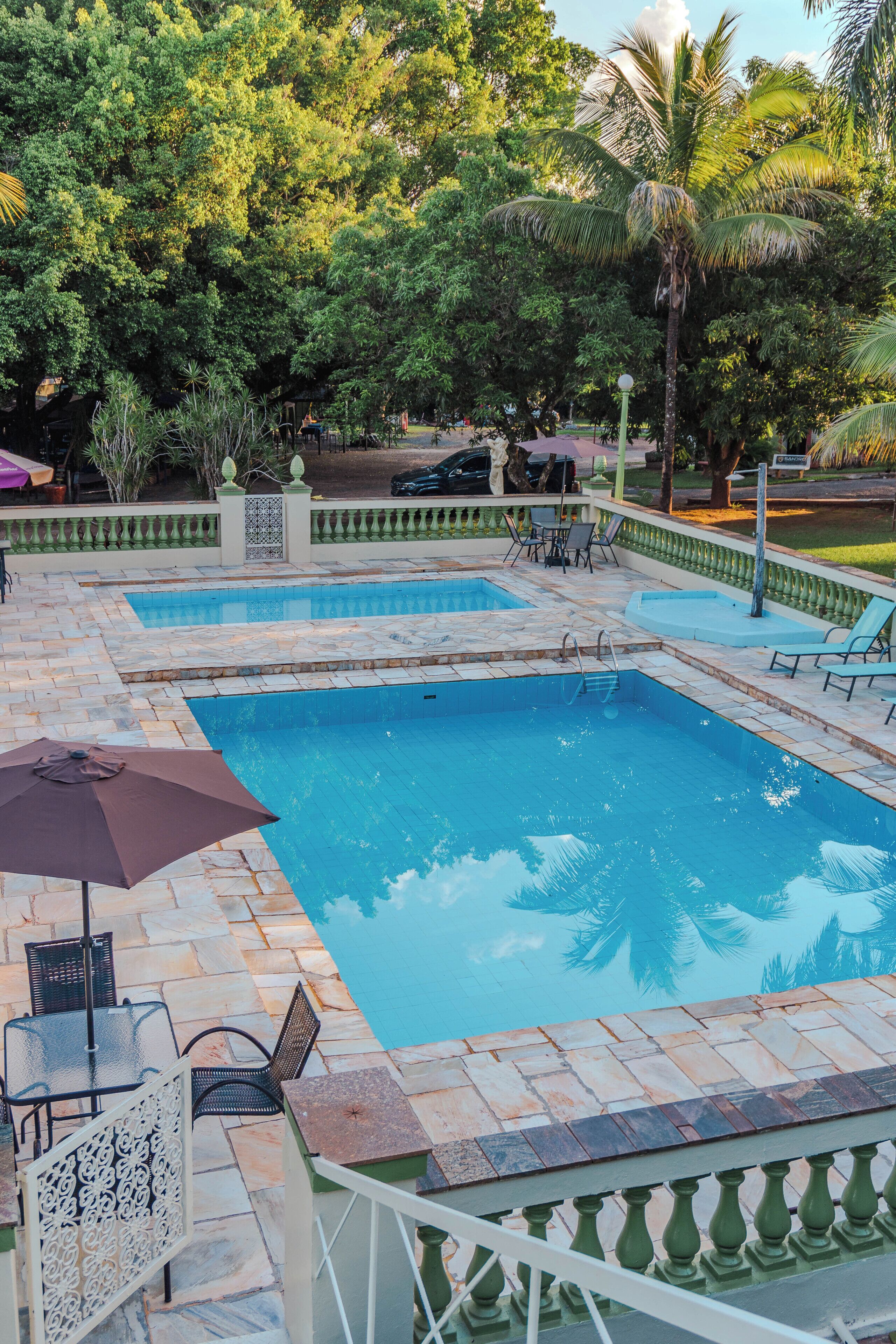 A rectangular pool with a tiled deck, surrounded by greenery and a fence.