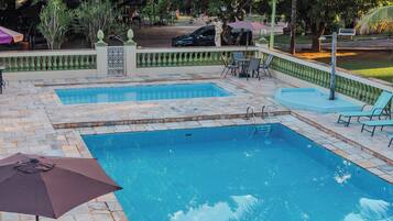 A rectangular pool with a tiled deck, surrounded by greenery and a fence.