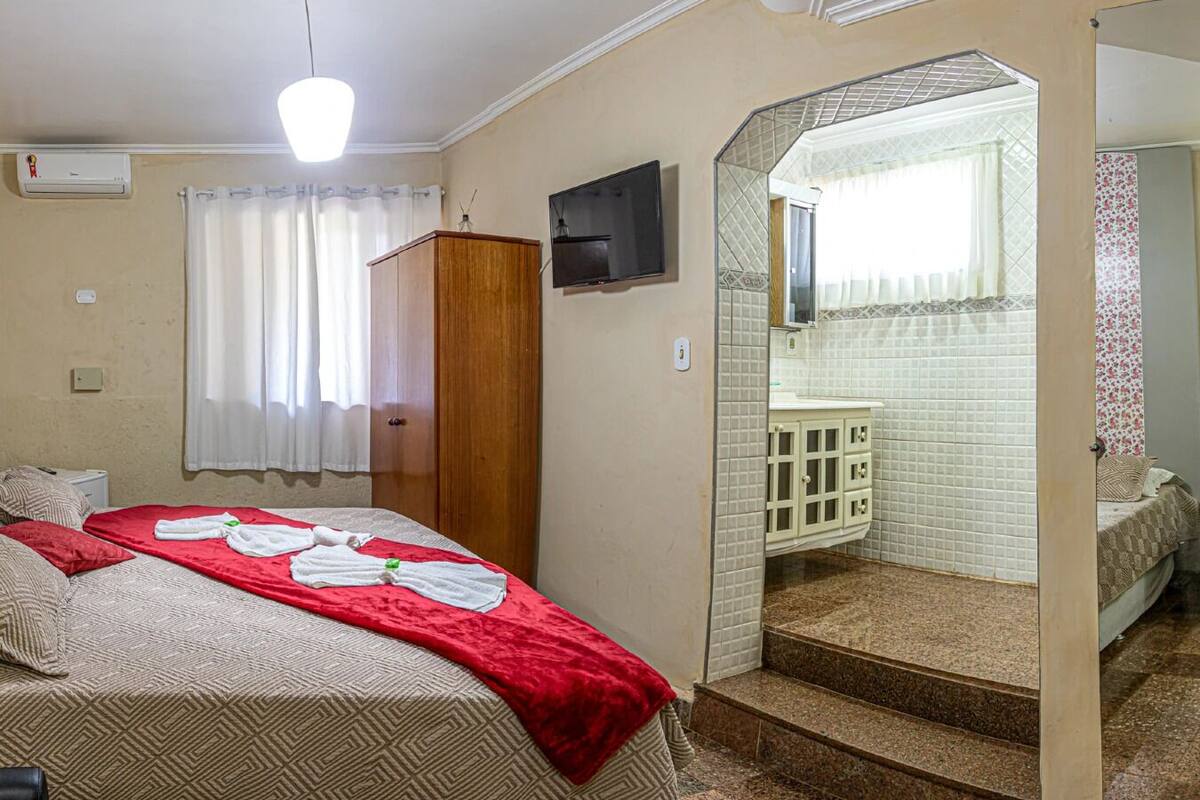 Ein Hotelzimmer mit Bett, Fernseher, Kleiderschrank und einem Badezimmer mit gefliestem Duschbereich.
