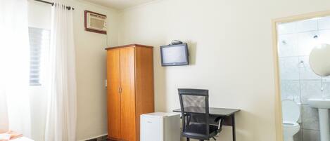 Una habitación con cama, escritorio y silla, armario, televisión y baño con lavamanos e inodoro.
