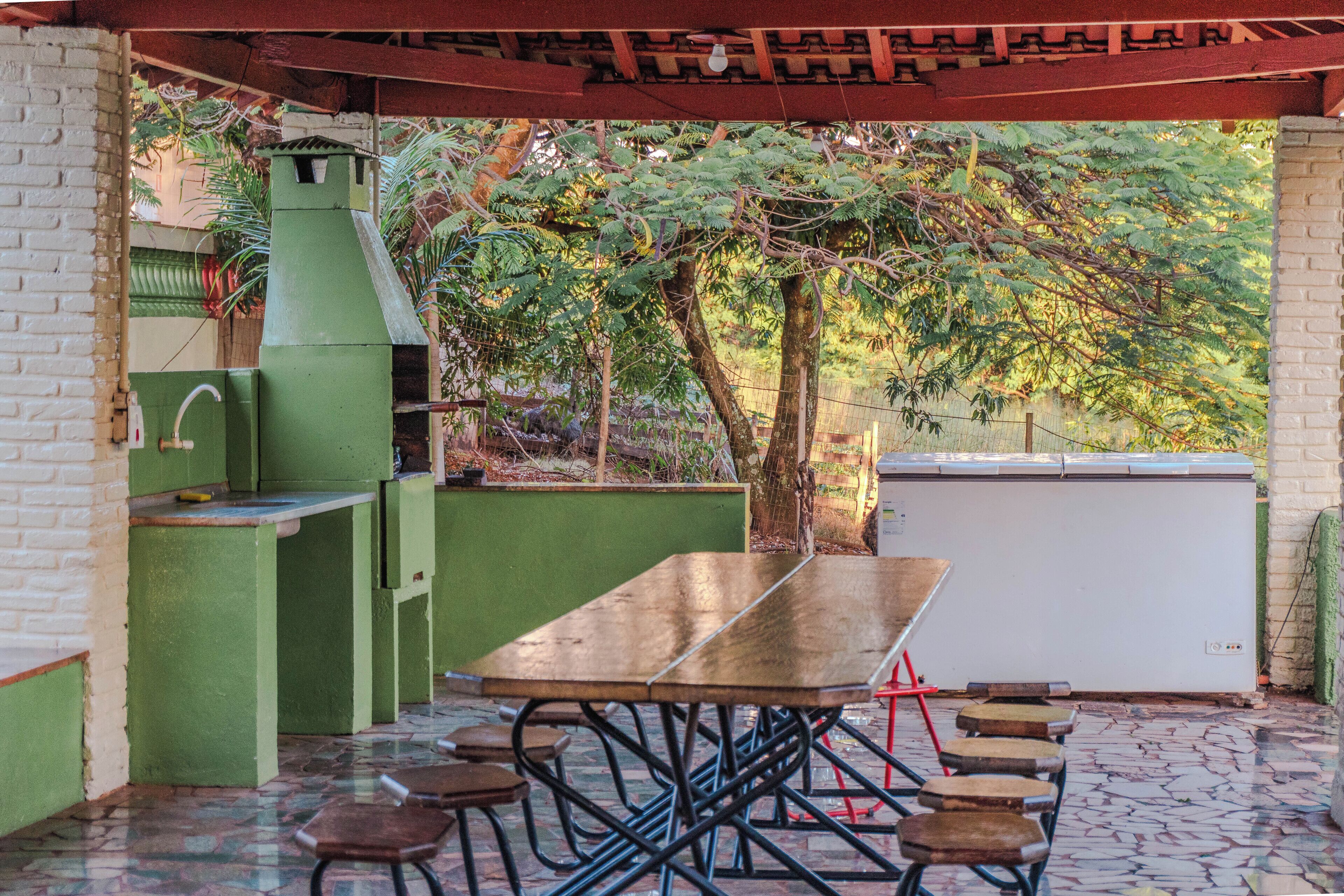 An outdoor patio with a wooden table and benches, a green barbecue grill, and a white refrigerator.