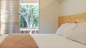 Een slaapkamer met een bed, een houten hoofdbord, een raam met uitzicht op bomen en een airconditioning.