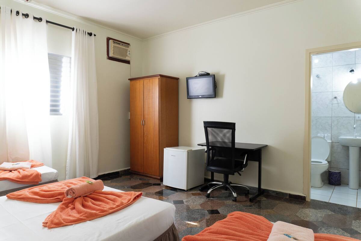 Ein Hotelzimmer mit zwei Betten, einem Schreibtisch, einem Fernseher, einem Kleiderschrank und einem durchgegangenen Tür erkennbaren Badezimmer.