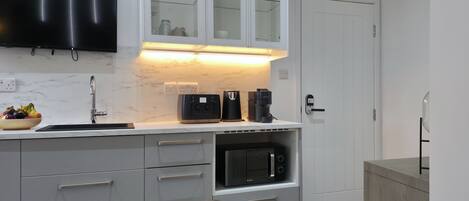 Una cocina moderna con microondas integrado, cafetera y frutero en la encimera.