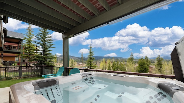 A hot tub with a control panel, a view of mountains, and a building with a balcony in the background. - Walk to Town | Hot Tub (Fraser)