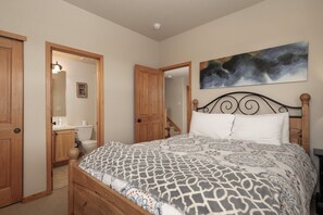 A bedroom with a bed, wooden doors, a bathroom, and a painting on the wall. - Escape in Style: Welcome to our Rendezvous Retreat (Fraser)