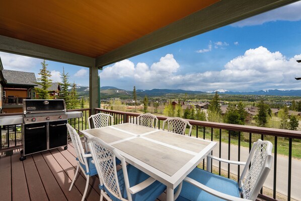 A covered outdoor deck with a wooden table and chairs, a grill, and a view of a mountainous landscape. - Escape in Style: Welcome to our Rendezvous Retreat (Fraser)