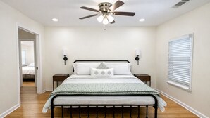 A bedroom with a bed, a ceiling fan, two bedside tables, a window with blinds, and a door leading to another room. - World Cup House ATL (Atlanta)