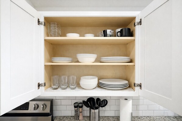 A kitchen cabinet with shelves holding plates, bowls, glasses, and a coffee maker.