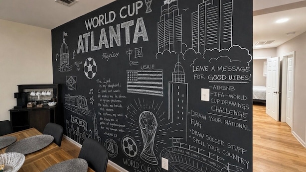 A room with a large wall mural featuring the World Cup and Atlanta, USA, with a dining area in the foreground. - World Cup House ATL (Atlanta)