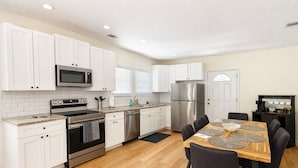 A modern kitchen with white cabinets, stainless steel appliances, and a dining area with a wooden table and chairs. - World Cup House ATL (Atlanta)
