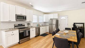 A modern kitchen with white cabinets, stainless steel appliances, and a dining area with a wooden table and chairs.