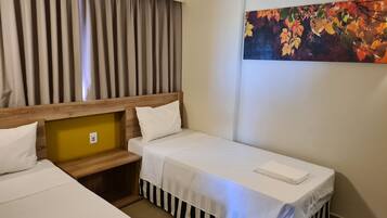 A hotel room with two single beds, a wooden headboard, a small wooden bench, and a colorful autumn leaf painting on the wall.