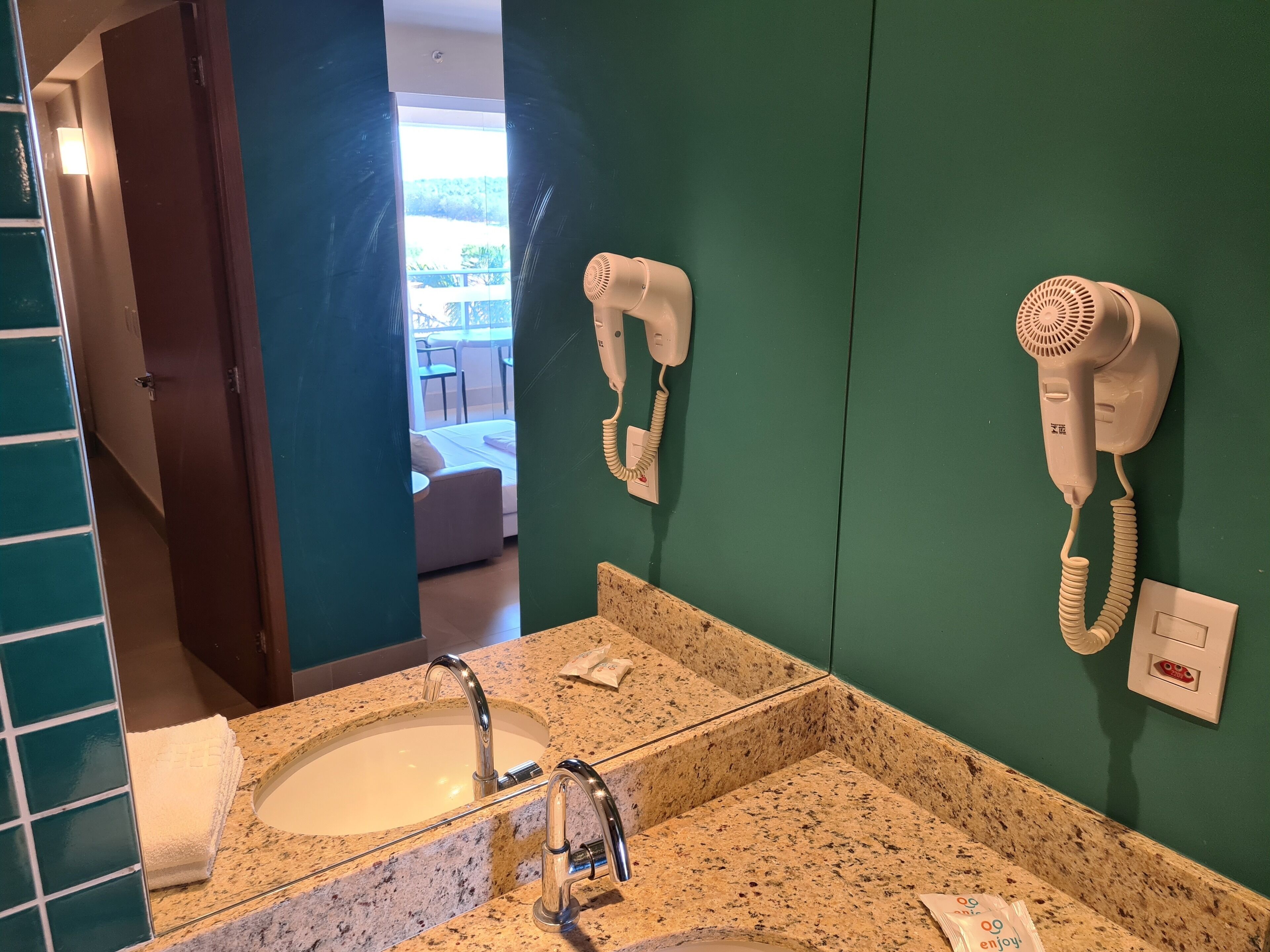Une salle de bain dotée d’un comptoir en granit, d’un lavabo et de deux sèche-cheveux fixés au mur.