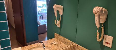 Une salle de bain dotée d’un comptoir en granit, d’un lavabo et de deux sèche-cheveux fixés au mur.