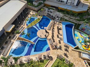 Une grande piscine extérieure dotée de plusieurs zones et d’un espace circulaire central, entourée de chaises longues et de parasols.