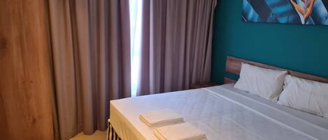 A hotel room with a bed, curtains, a wooden headboard, and a wall art piece.