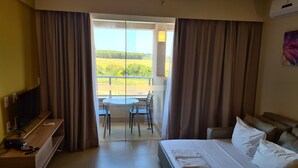 A hotel room with a bed, a TV, a desk with a phone, and a balcony with a table and chairs. - Hospede-se no Solar das Águas (Olímpia)