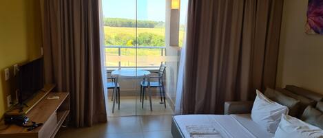 A hotel room with a bed, a TV, a desk with a phone, and a balcony with a table and chairs.