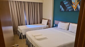 A hotel room with two beds, a large window with curtains, a teal accent wall, and a painting above the beds. - Hospede-se no Solar das Águas (Olímpia)