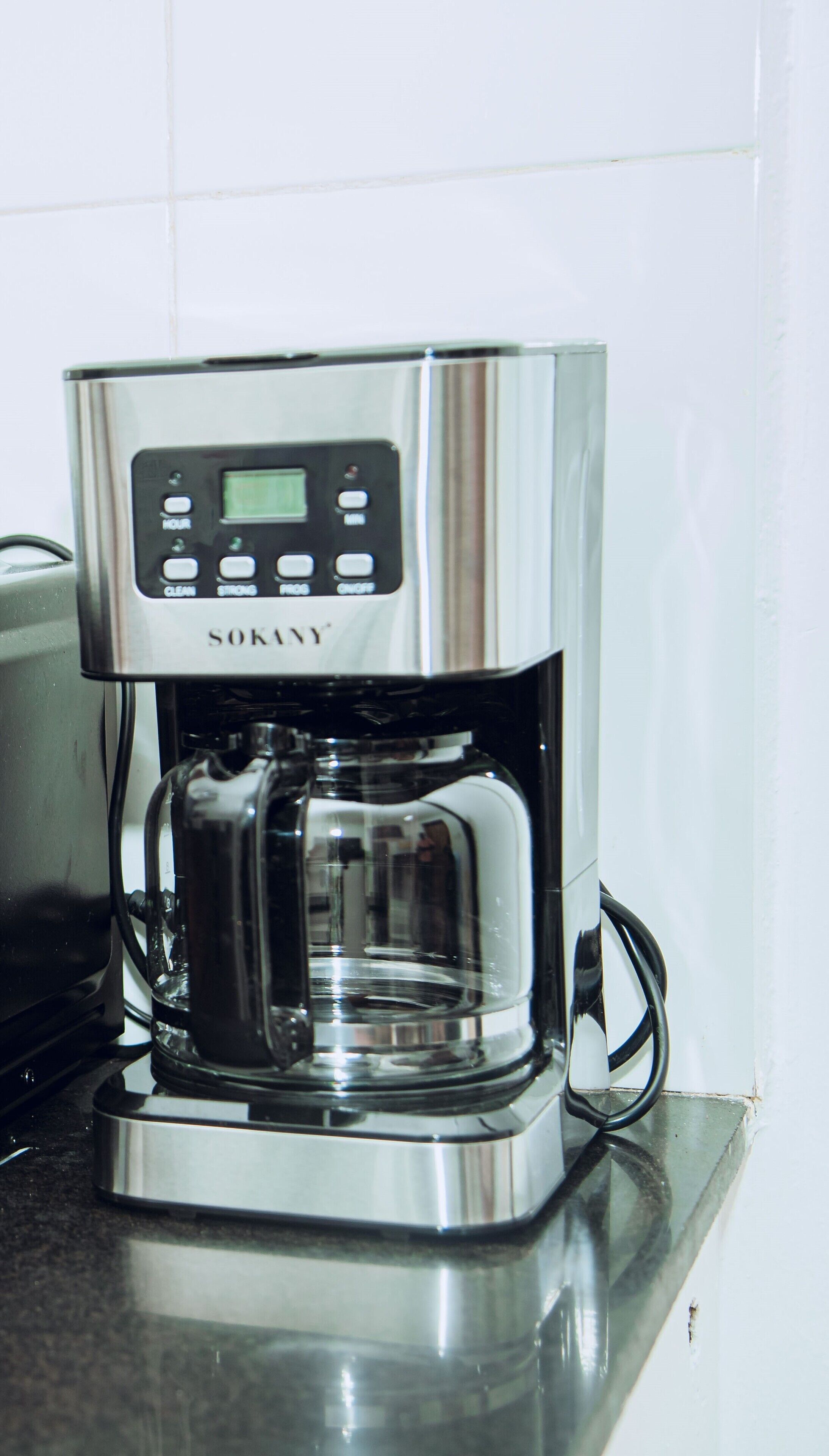 Una cafetera de acero inoxidable con pantalla digital y botones de control, ubicada sobre una encimera de cocina.