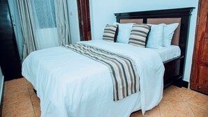 A neatly made bed with a striped blanket, a wooden headboard, and a plain white wall.