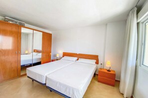 Ein Schlafzimmer mit einem Doppelbett, einem Kleiderschrank, einem Nachttisch mit Lampe und einem Fenster mit Vorhängen.