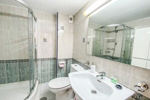 Ein modernes Badezimmer mit einer Duschkabine, einer weißen Toilette und einem großen Waschbecken mit Spiegel darüber.