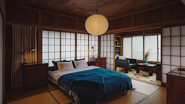Une chambre de style japonais traditionnel, avec un sol recouvert de tatamis, un lit avec une couverture bleue, une lanterne en papier suspendue et des portes coulissantes de type shoji.
